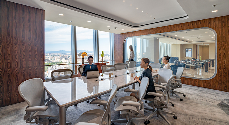 A 12-pax meeting room with a large window, featuring four women seated around a table with laptops during a meeting