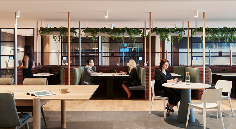 A modern coworking space in Australia featuring long and round tables, booths, and people engaged in work and meetings