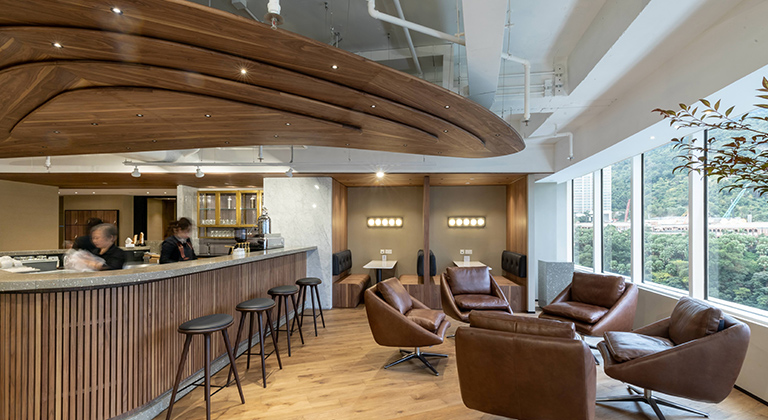 A modern office featuring a curved ceiling, wooden floors, lounge area, barista bar, and a view of the city skyline