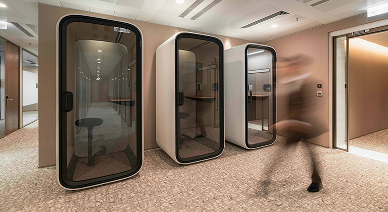 A professional walks through an office space featuring several phone booths in the background