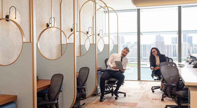 Two individuals working at desks in a coworking space, with a panoramic view of the city skyline in the background